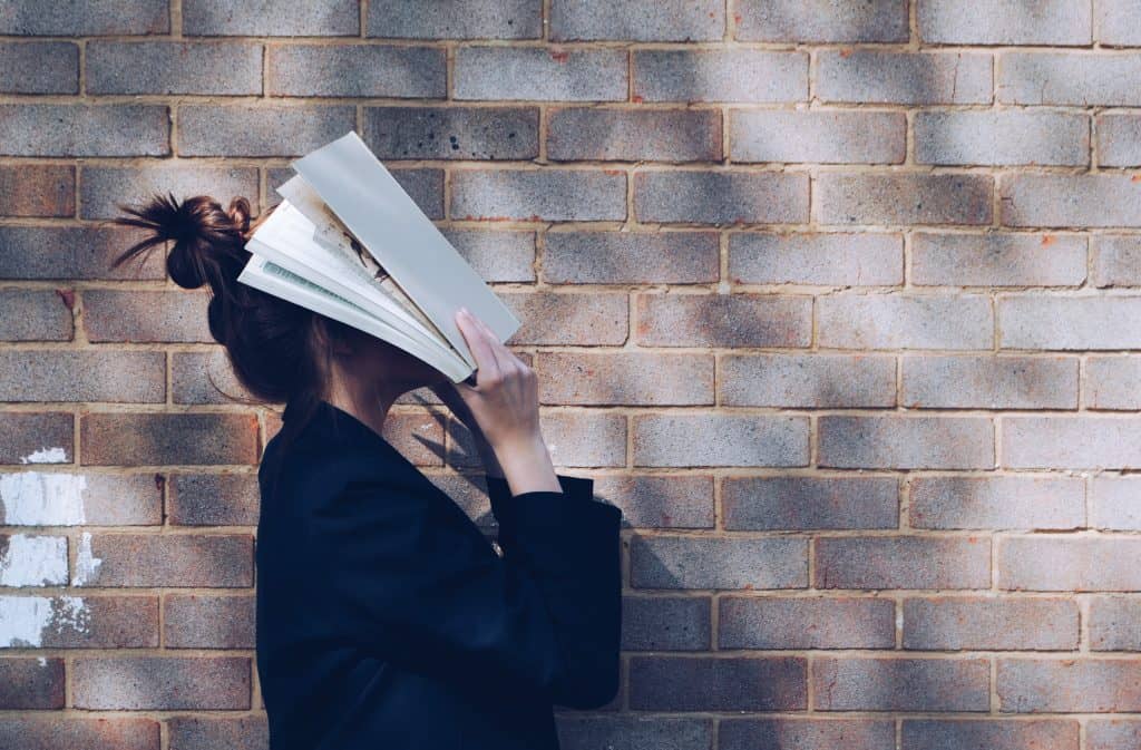 Teen girl with book over her head standing against a wall