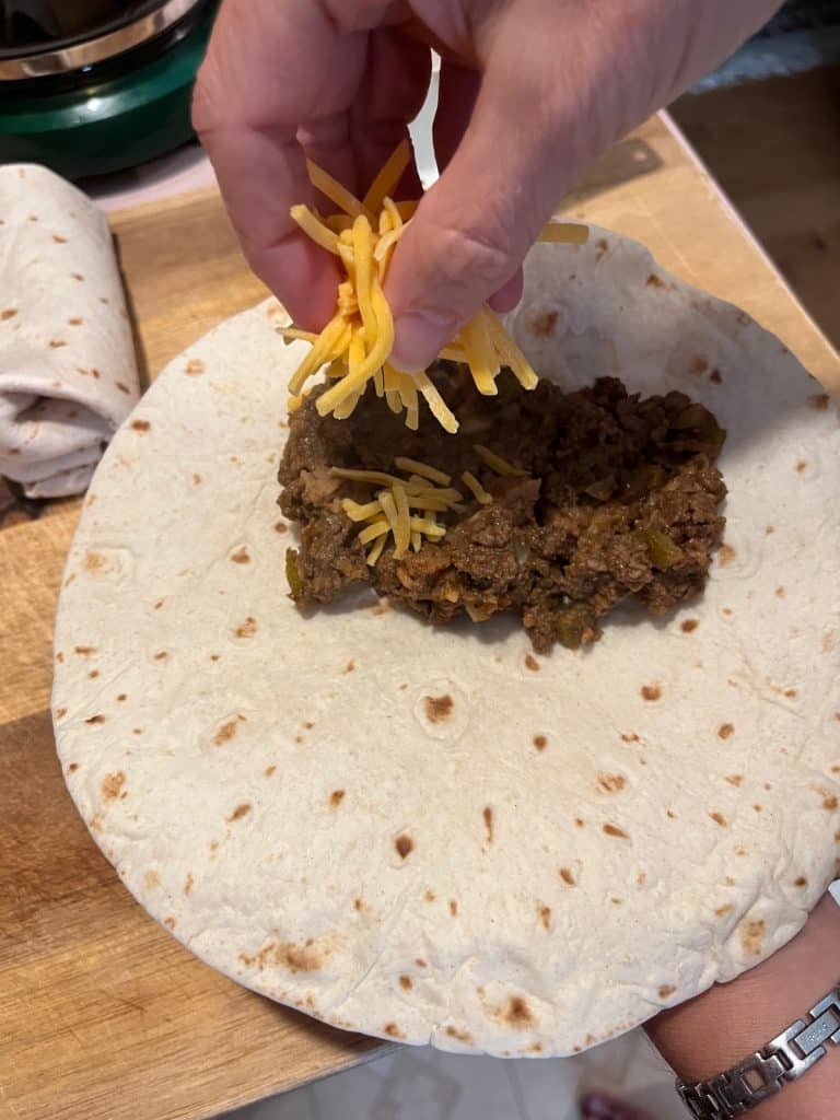 open tortilla with beef mixture and adding shredded cheese