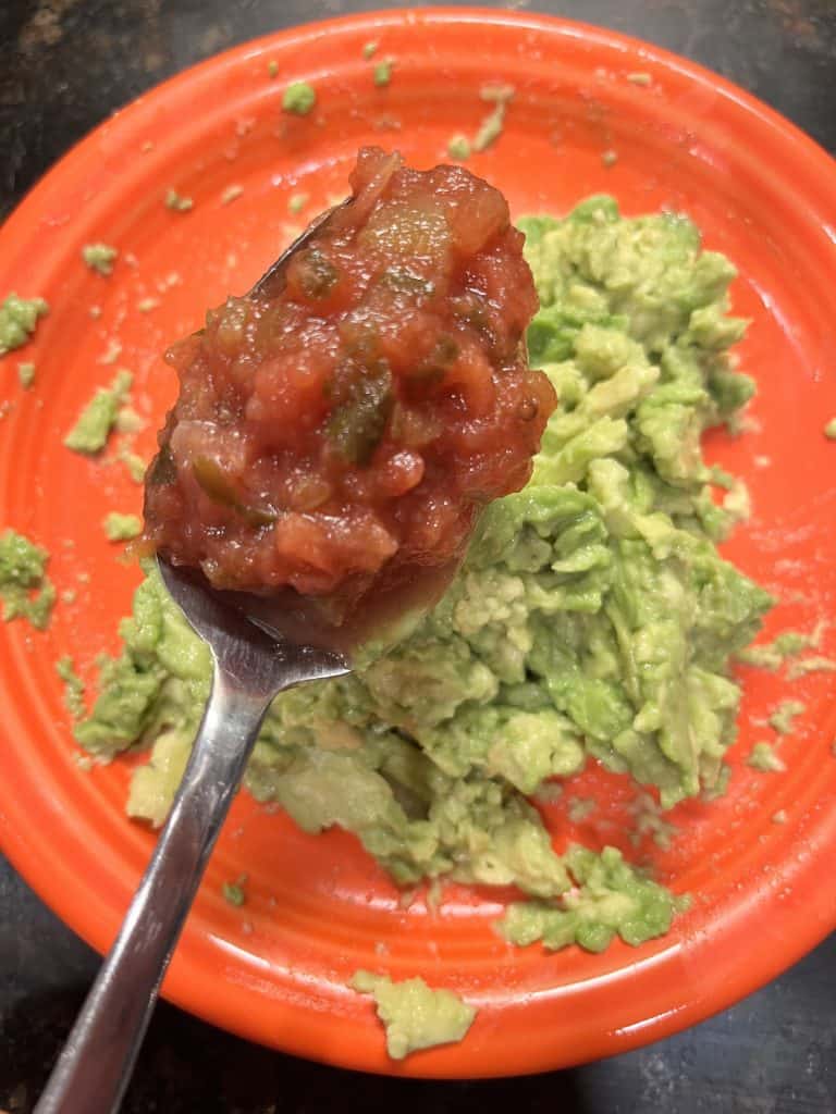 Spoonful of salsa being put onto mashed avocado