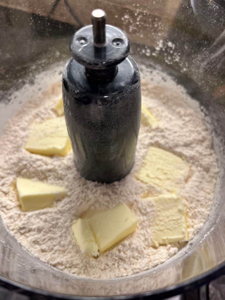 Close up of pieces of butter on dry ingredients in food processor.