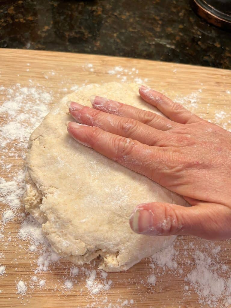 Hand patting down biscuit dough on floured surface.