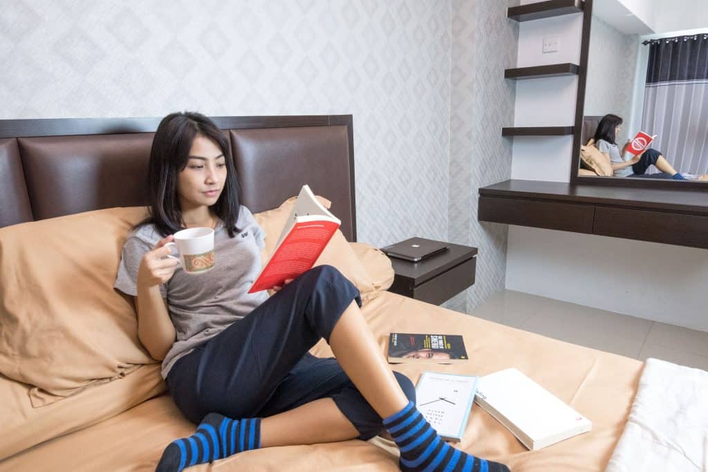 Woman sitting on bed reading and holding a cup of tea