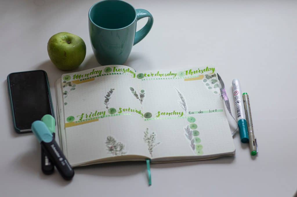 Weekly planner with coffee cup and apple beside planner