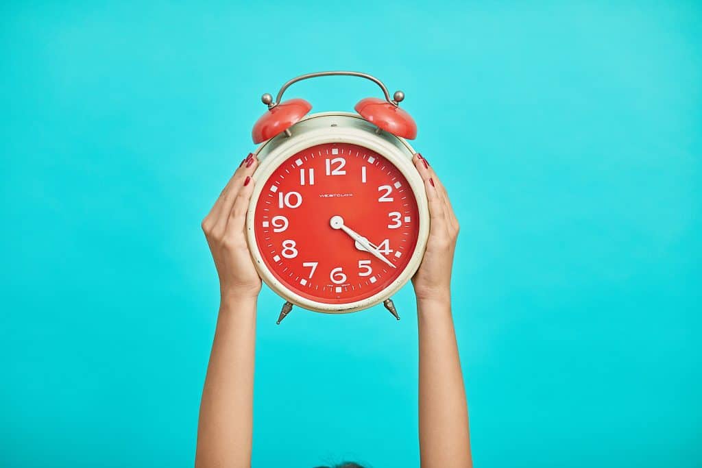 Woman's hands holding up large red alarm clock with blue background.