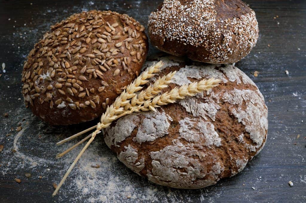 three round dark bread loaves with stalk of wheat on top