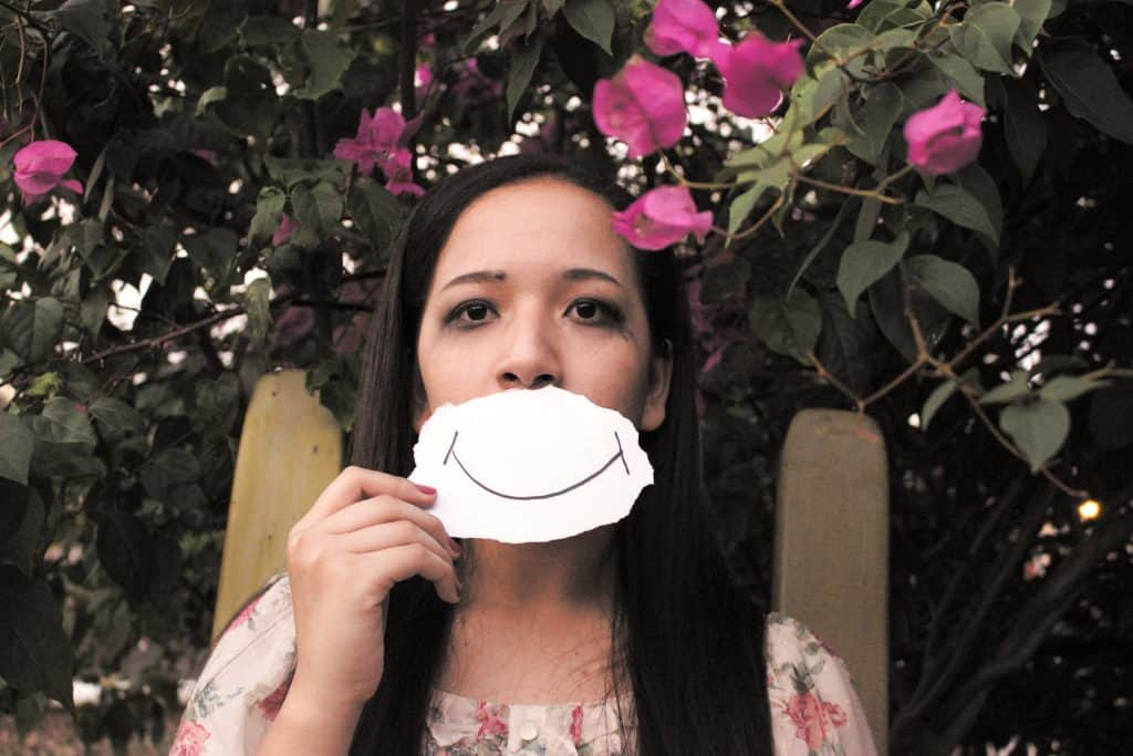 sad lady holding picture of smiley face over mouth