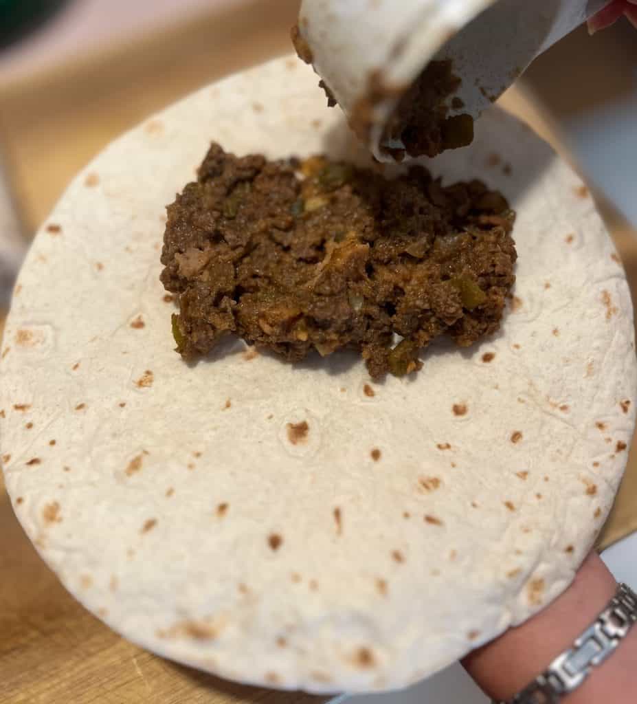 tortilla with beef filling being spread on open tortilla