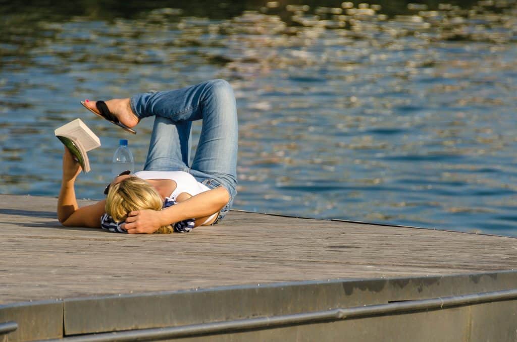 woman lying on dock at lake holding a book